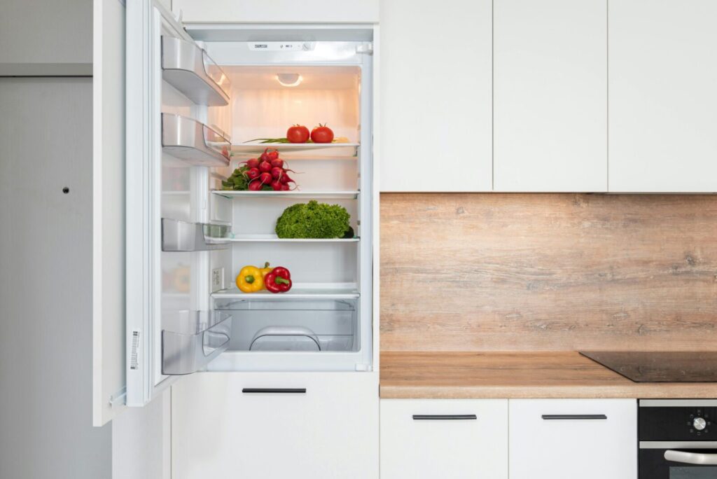Contemporary kitchen with refrigerator filled with fresh bright tomatoes lettuce and bell peppers