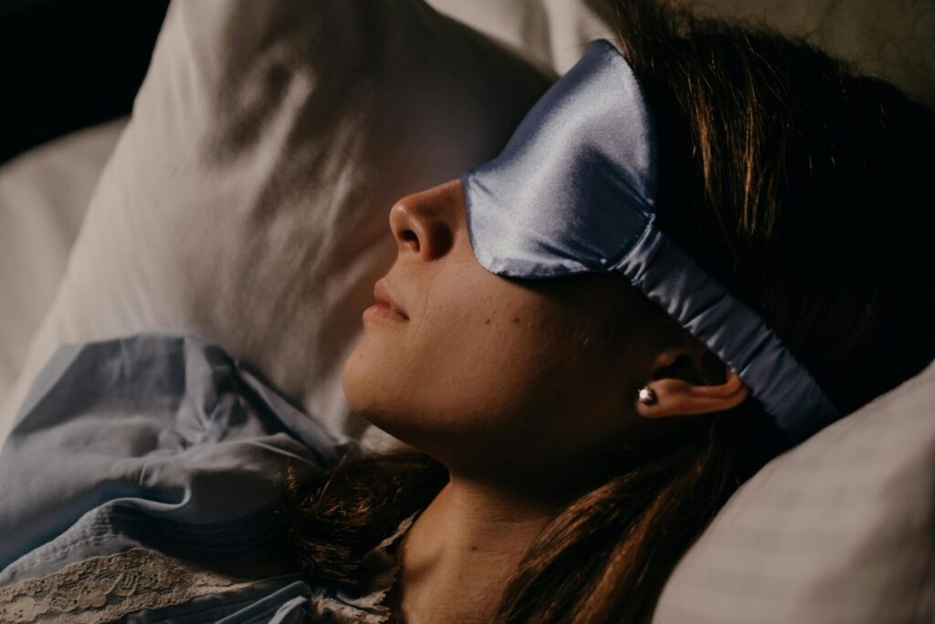A woman peacefully sleeping on a pillow with a blue silk eye mask, indoors.
