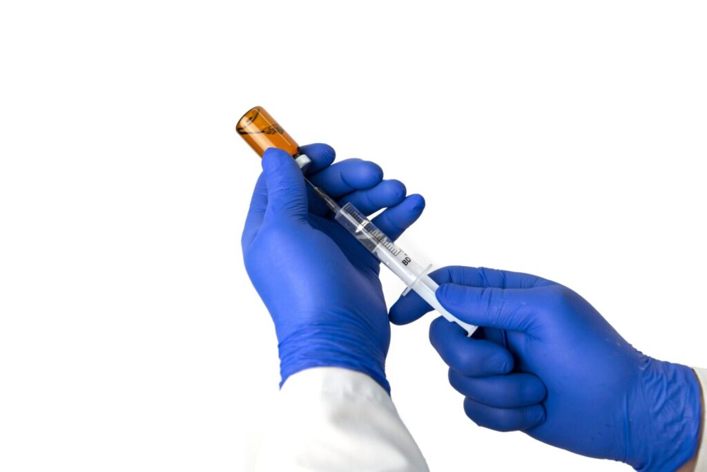 Unrecognizable medic in blue protective gloves with bottle of drug filling syringe with vaccine against white background during coronavirus pandemic