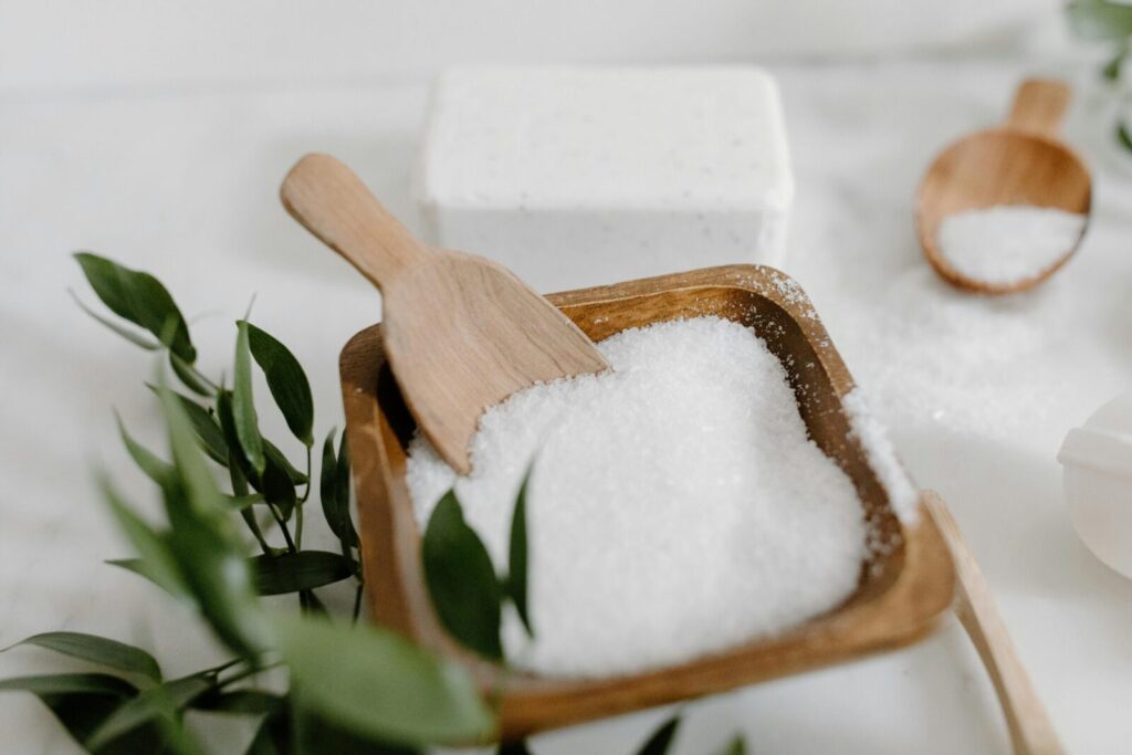 A minimalist display of coarse white salt in a wooden bowl with scoops on a marble surface.