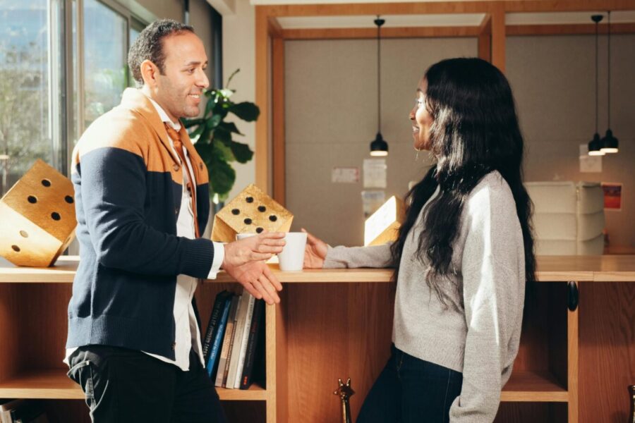 Two colleagues engaging in a friendly conversation in a modern office setting, promoting cooperation and teamwork.