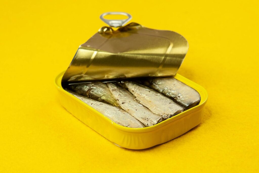 Close-up of an open sardine can on a vibrant yellow background, suitable for ads.