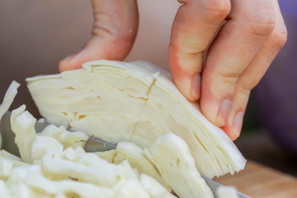 Crop unrecognizable chef chopping fresh ripe cabbage on wooden cutting board against blurred background