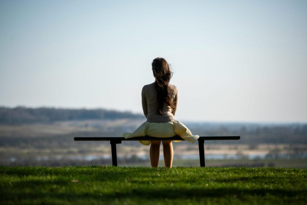 Serene image of a woman sitting on a bench overlooking a scenic field, symbolizing solitude and reflection.