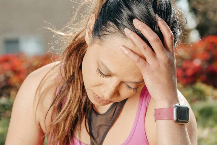 Close-up of a woman with a headache sitting outdoors wearing a smartwatch.