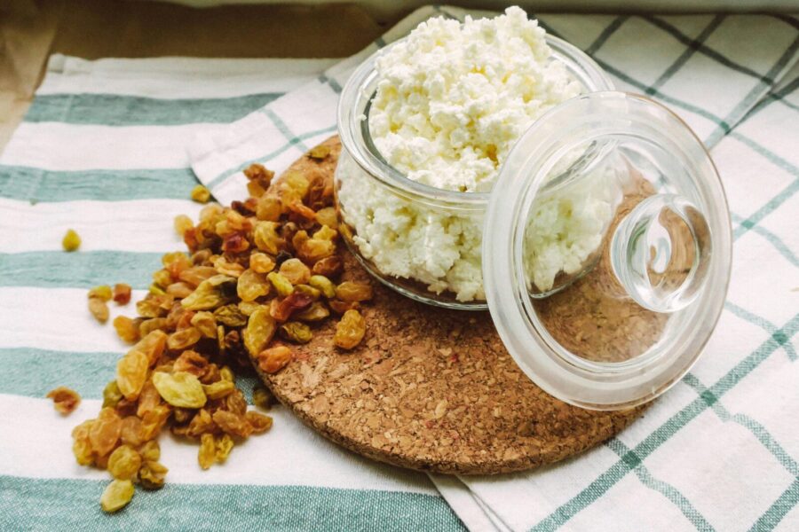 A close-up of cottage cheese in an open glass jar with scattered raisins on a cloth surface.