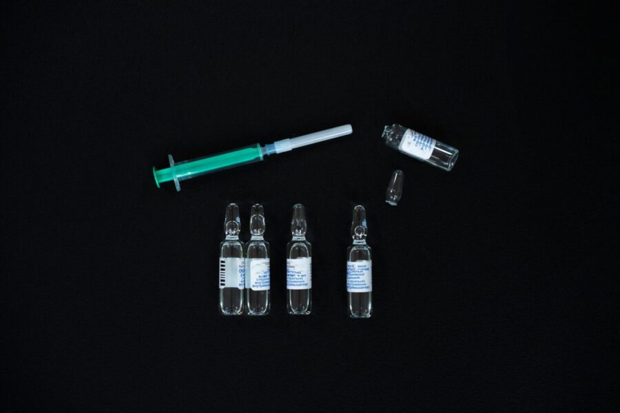 A close-up view of glass ampoules and a syringe on a black background, representing medical supplies.