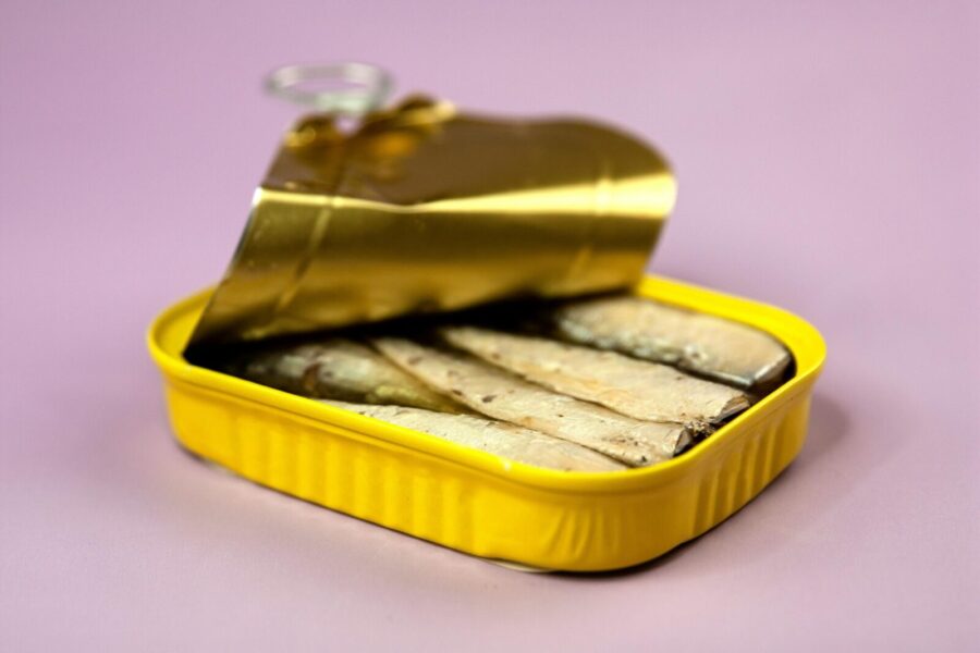 Opened delicious canned sardines in yellow container with oil on centre of light purple background