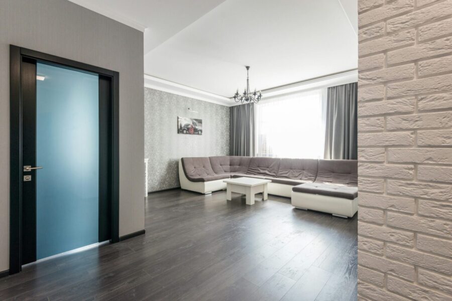 View of empty spacious living room with wooden floor and big comfortable sofa with beige seats and white coffee table near and picture hanging on wall