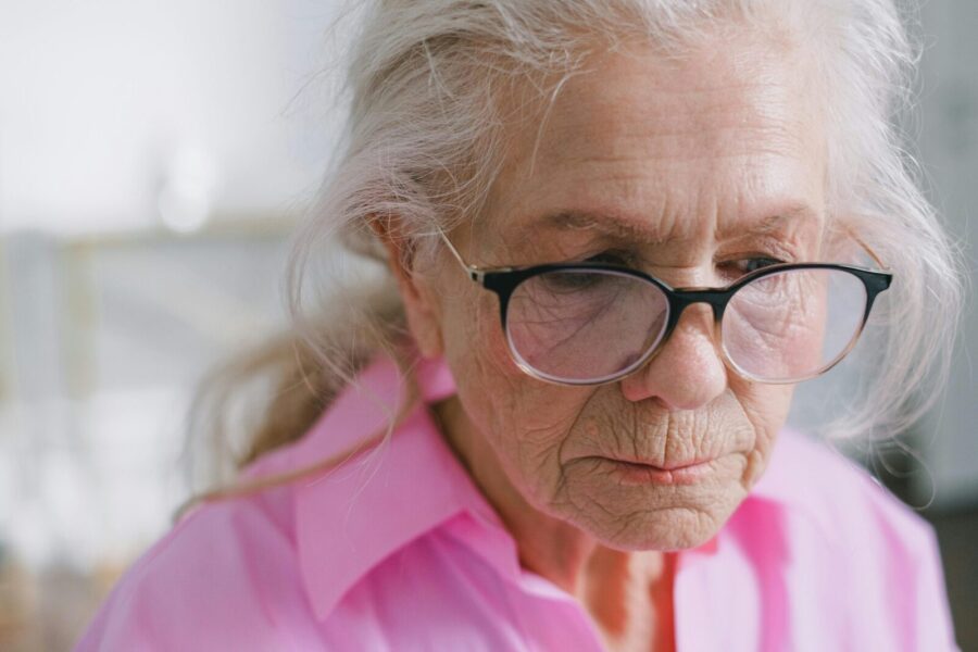 Close-up of an elderly woman with eyeglasses in a thoughtful pose indoors.