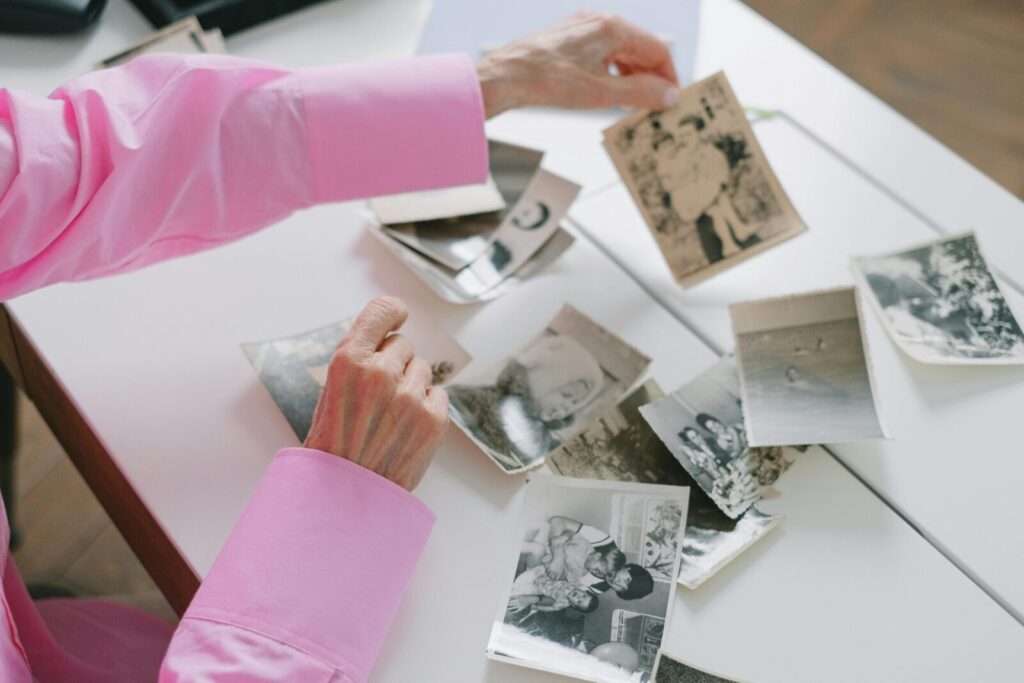 An elderly woman in a pink shirt sorting through old black and white family photographs, evoking nostalgia.
