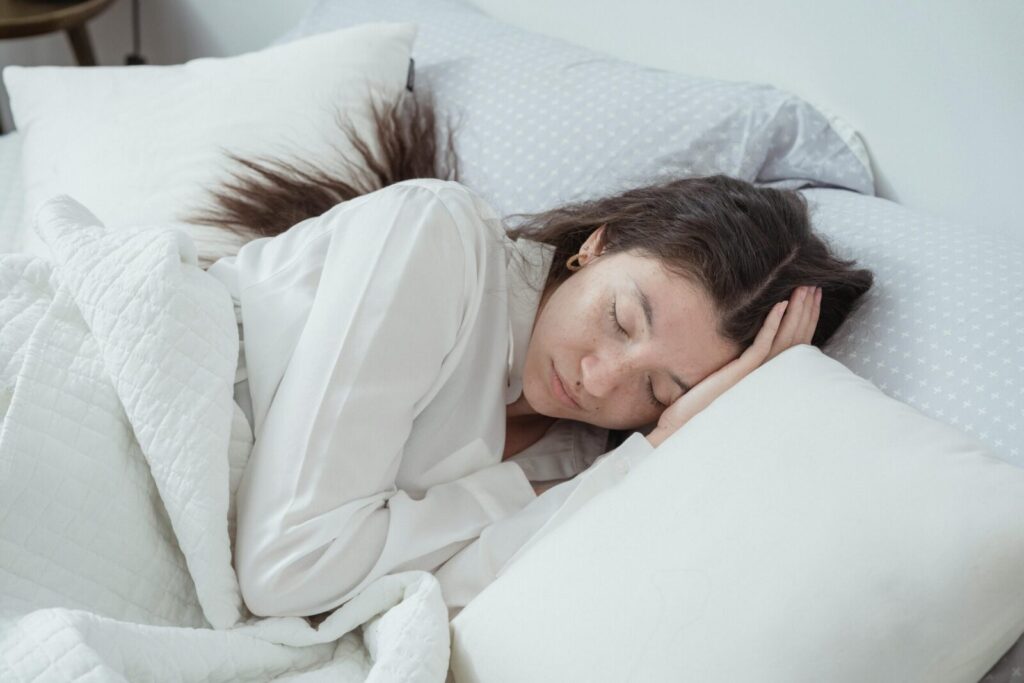 A serene woman rests comfortably in bed with soft pillows and blankets, embracing relaxation.