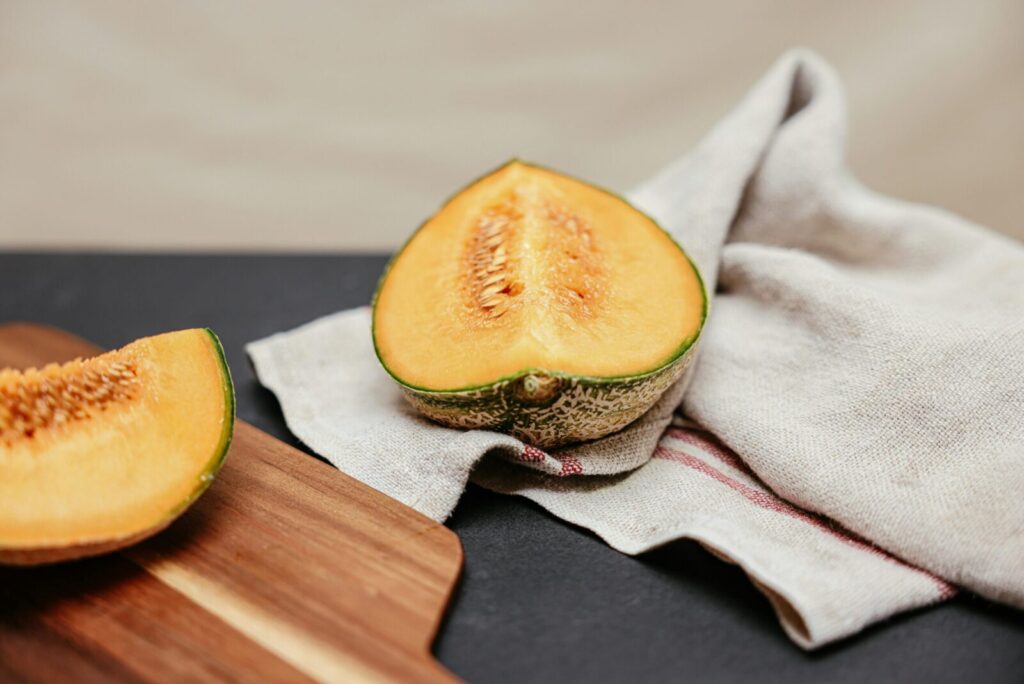 Close-up of sliced cantaloupe on a wooden board with linen cloth, highlighting fresh textures.