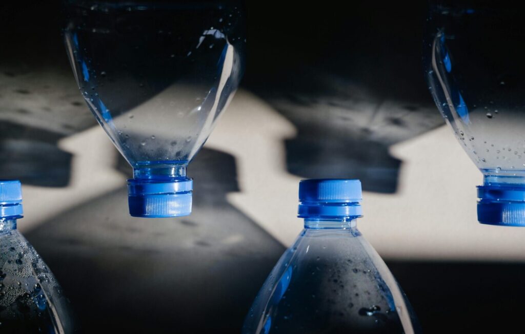 Close-up of plastic bottles with blue caps casting shadows, highlighting recycling themes.