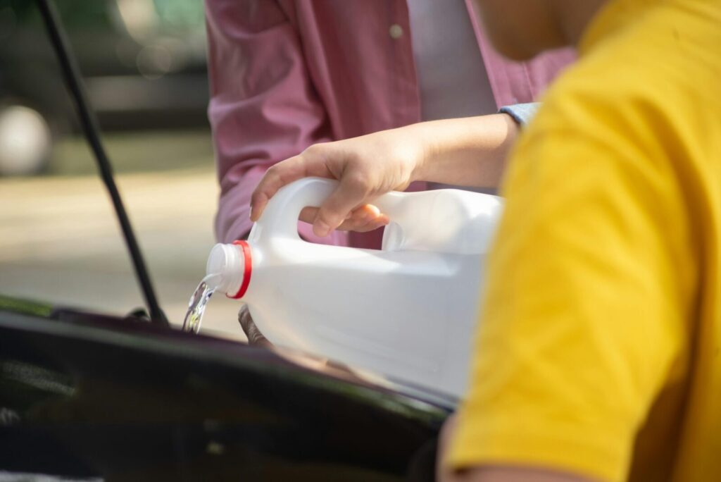 Close-up of hands pouring water into a car engine, focusing on auto maintenance.