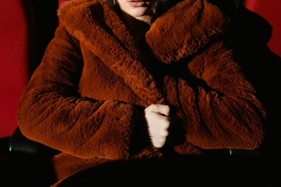 Close-up of a person warmly wrapped in a plush brown fur coat, seated indoors.