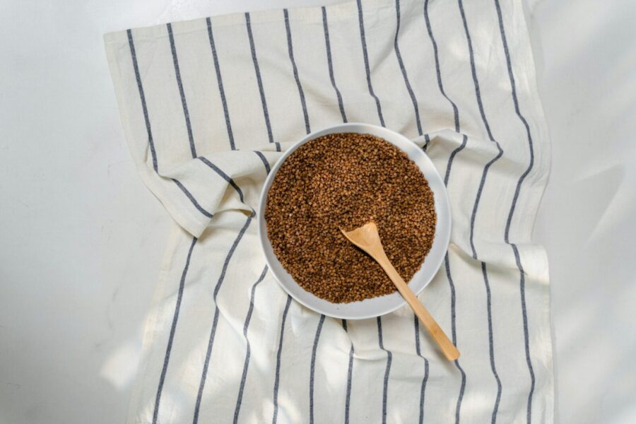 A ceramic bowl filled with raw buckwheat on a striped cloth, perfect for healthy cooking concepts.