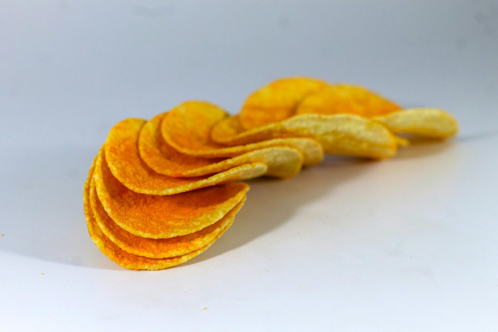 A detailed close-up of crunchy potato chips arranged in a curve on a white background.