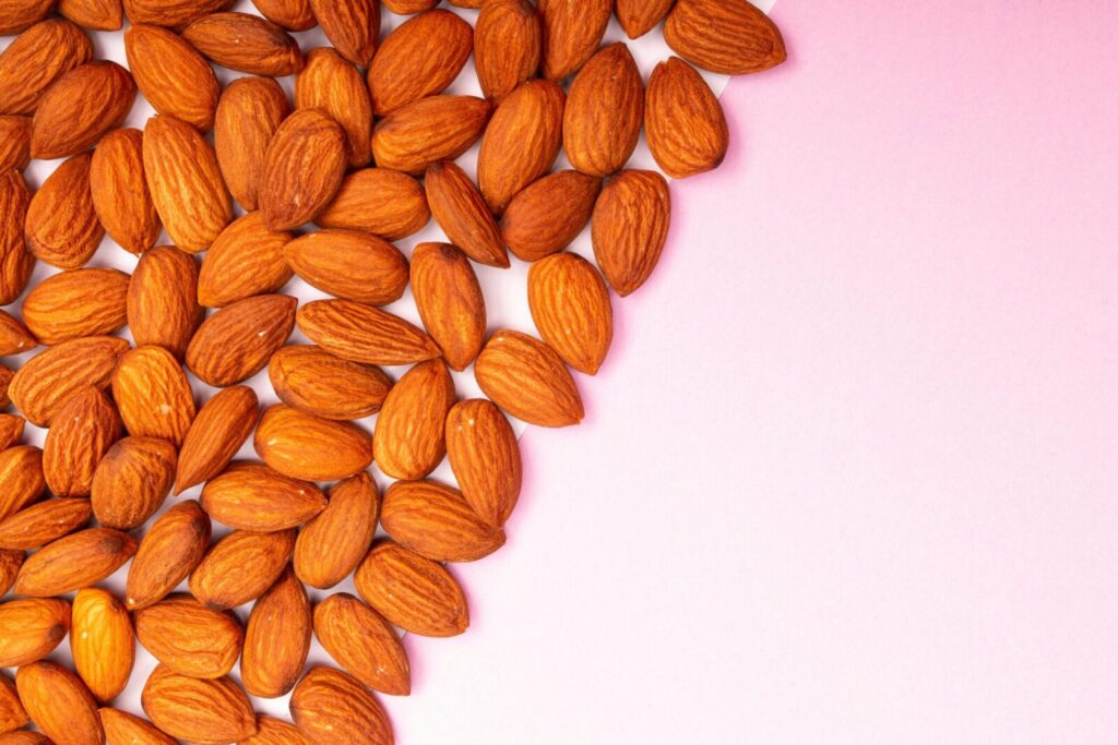 A vibrant close-up of roasted almonds artfully arranged on a pink background.