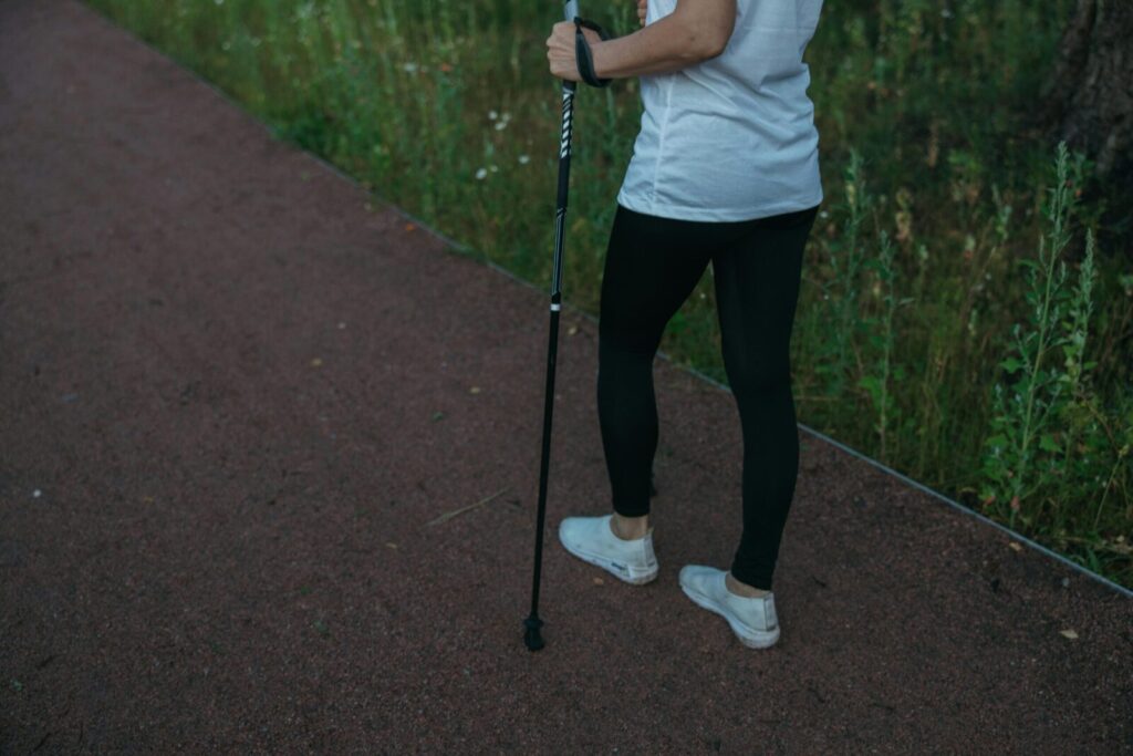 A person in athletic wear uses a trekking pole while walking on a forest pathway.