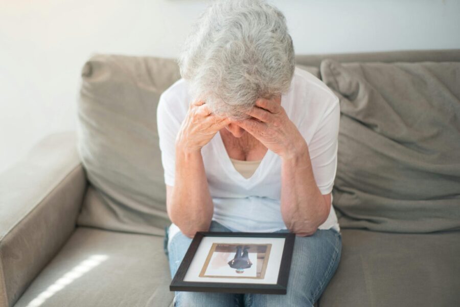 Senior woman sitting on couch, holding picture frame, looking melancholic.