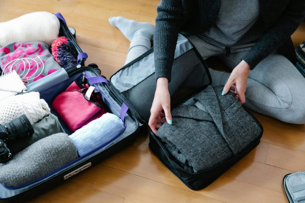 Woman organizes clothing and camera gear in a suitcase for travel.