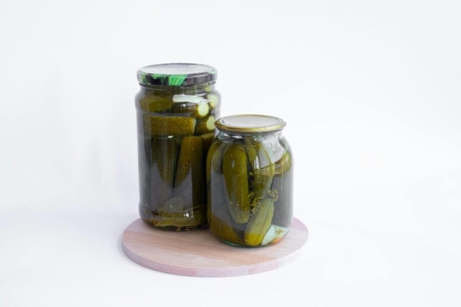 Two jars of pickled cucumbers placed on a wooden chopping board with a white background.