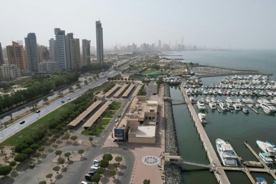 Aerial view of Kuwait City's modern skyline and bustling harbor with yachts.