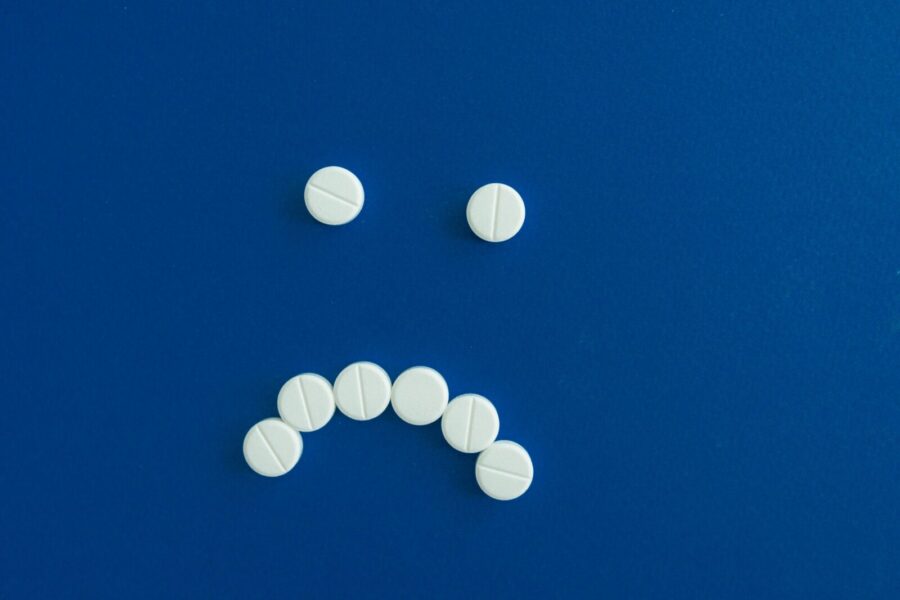 White pills arranged in a sad face shape on a solid blue background.