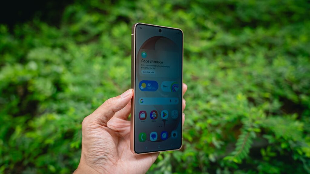 Hand holding a smartphone with green foliage background.