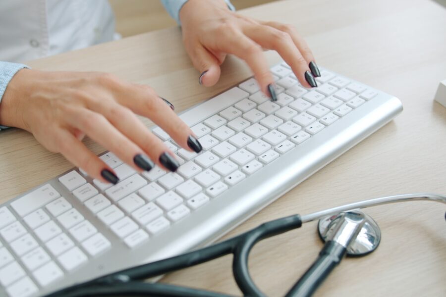 Doctor typing on keyboard with stethoscope nearby