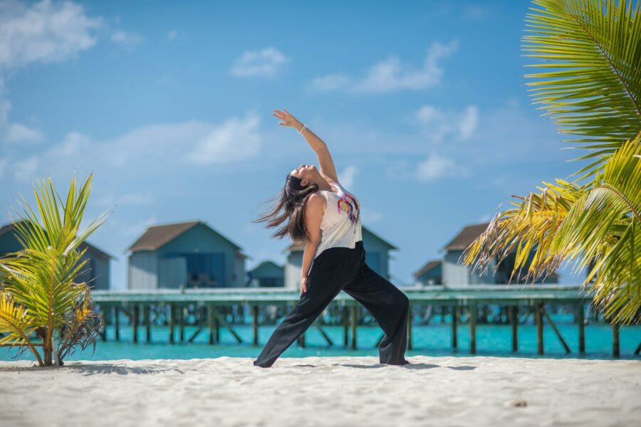 Woman practicing yoga on a sandy beach by the ocean.