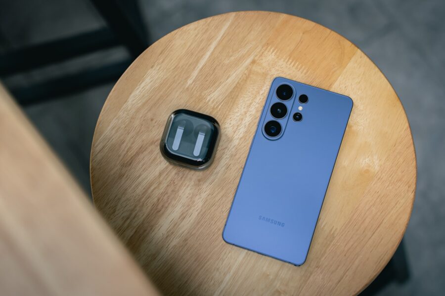 A blue smartphone and earbuds on a wooden table