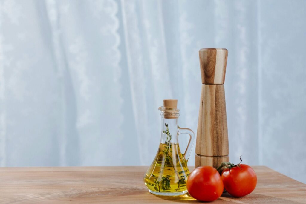 Fresh ingredients including olive oil, tomatoes, and a pepper mill on a kitchen table.