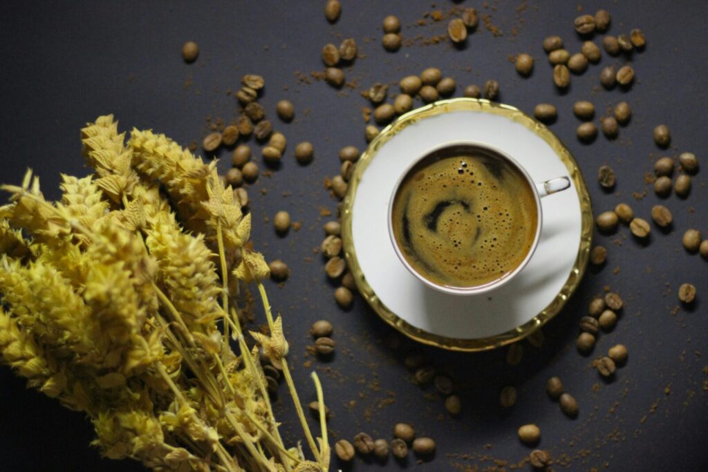 Stylish flatlay featuring a coffee cup, beans, and dried wheat on a dark surface.