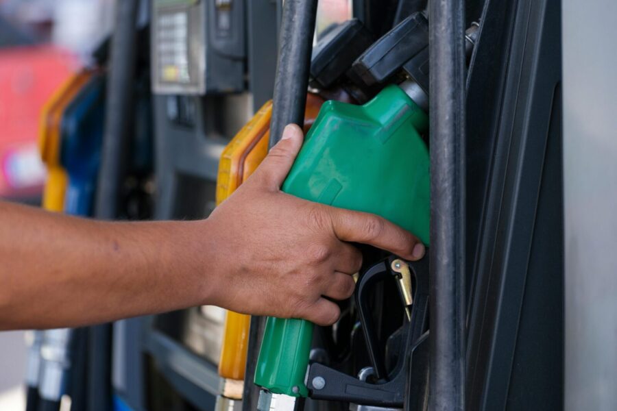 Close-up of a hand holding a green fuel nozzle at a gas pump station outdoors.