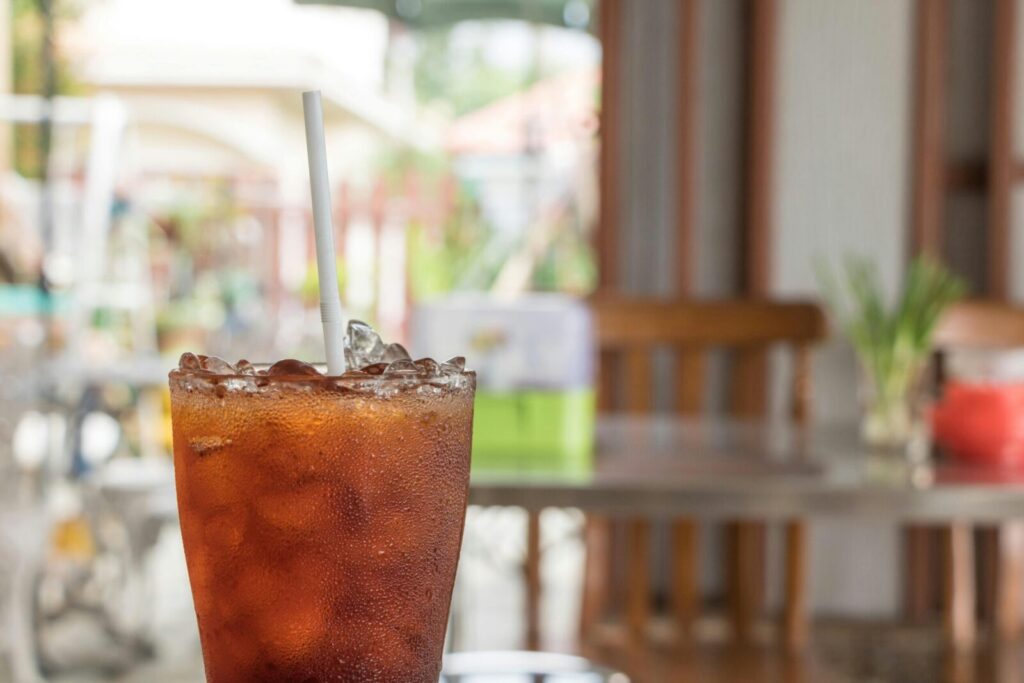 Refreshing glass of iced tea with a straw on a table in an outdoor cafe setting.