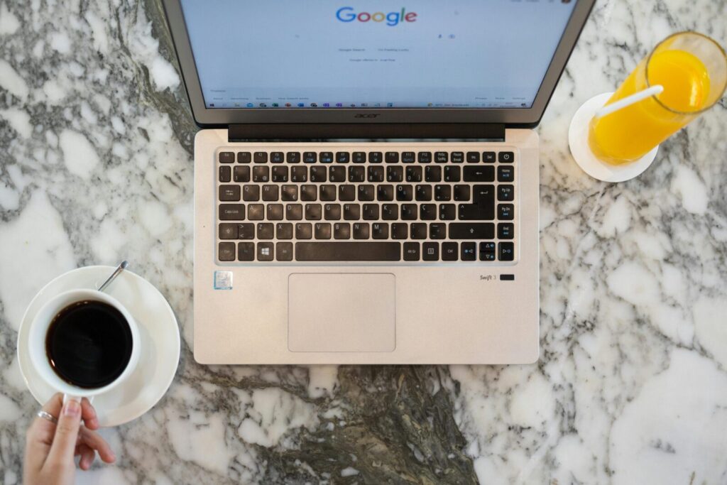 Top view of a laptop workspace with coffee and orange juice on a marble table. Perfect for productivity themes.