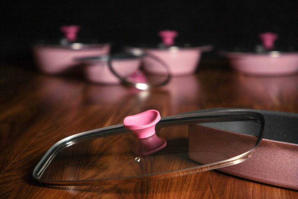 Elegant pink cookware with glass lids on a wooden surface, perfect for modern kitchen decor.