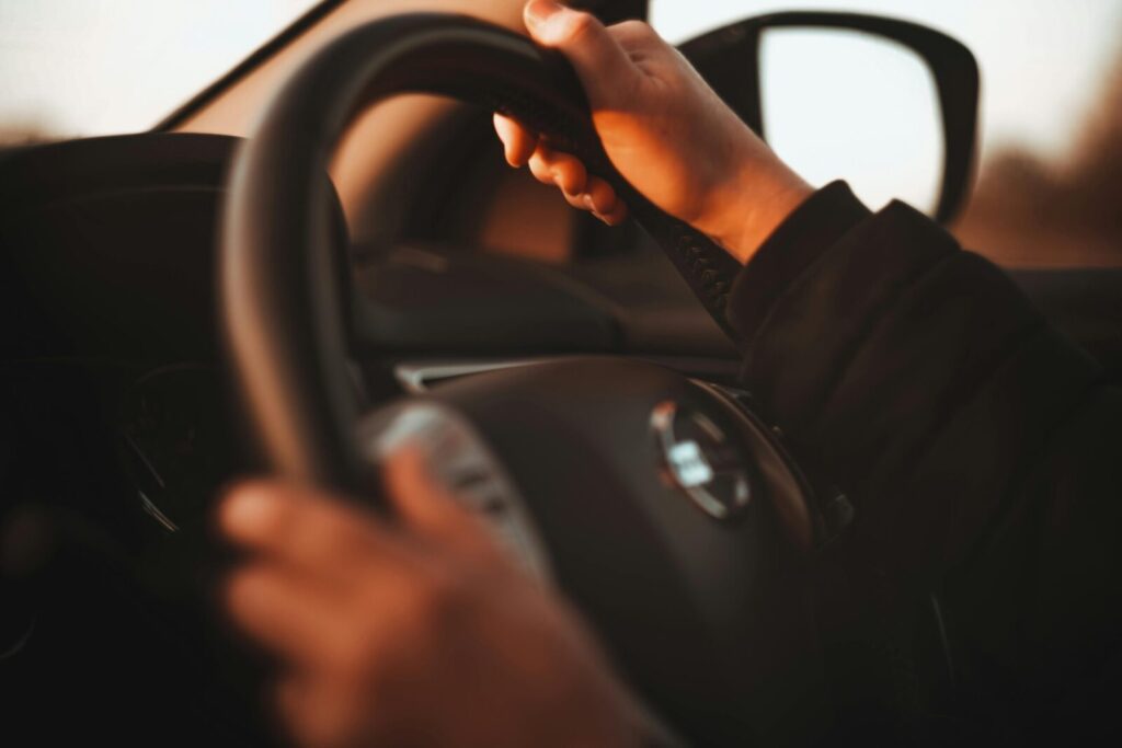 Close-up of a person's hands gripping a steering wheel in warm sunset light. Interior car focus.