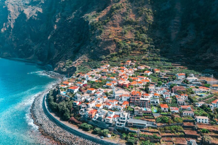 Stunning aerial view of a coastal town in Madeira, Portugal, with lush cliffs and turquoise sea.