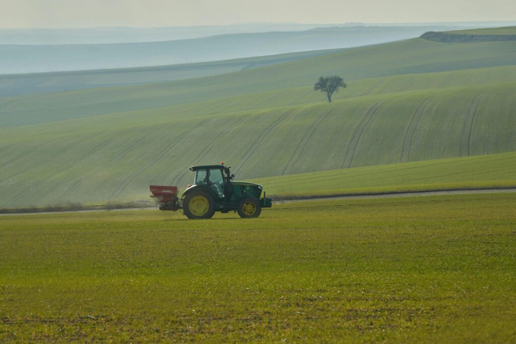 A single tractor traverses rolling green fields under a serene sunset sky.