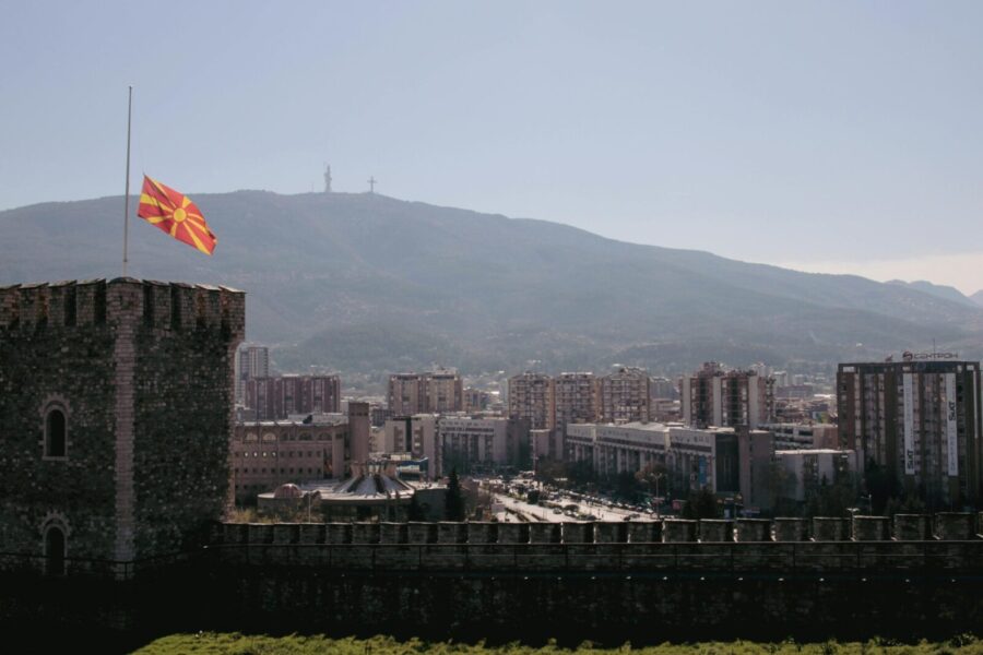 Scenic view of Skopje cityscape featuring the Macedonian flag and mountainous backdrop.