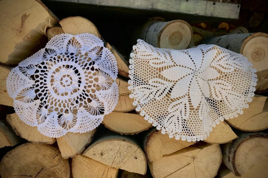 Beautiful crochet doilies displayed on stack of firewood, showcasing craftsmanship.