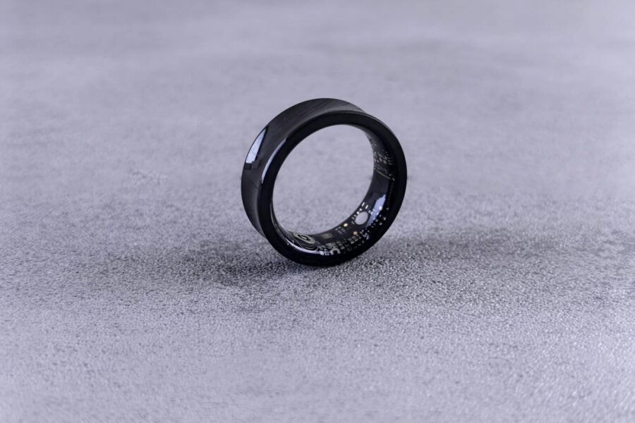A modern black smart ring with visible circuitry resting on a textured concrete surface.