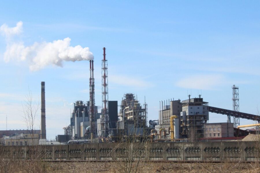 An industrial factory with smoke emissions against a clear blue sky.