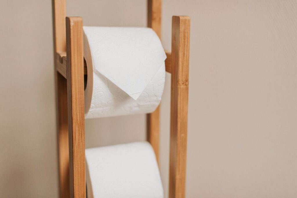 Wooden rack holding two toilet paper rolls in a minimalistic bathroom setting.