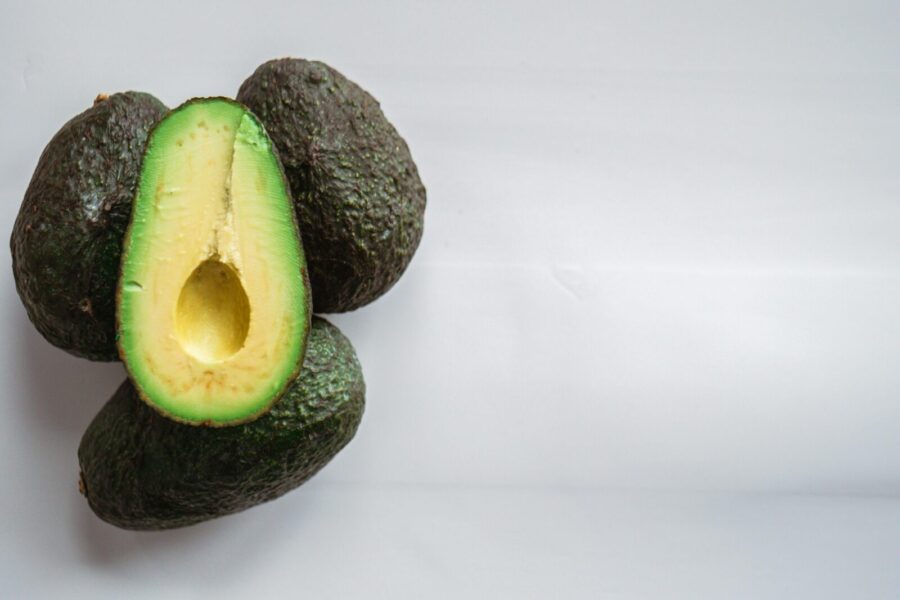 Top view of heap of fresh avocados with rough dry skin and colorful tender pulp on white background