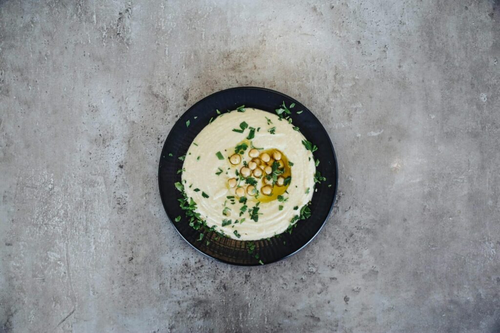 A flat lay of a plate of hummus garnished with chickpeas and herbs on a gray background.