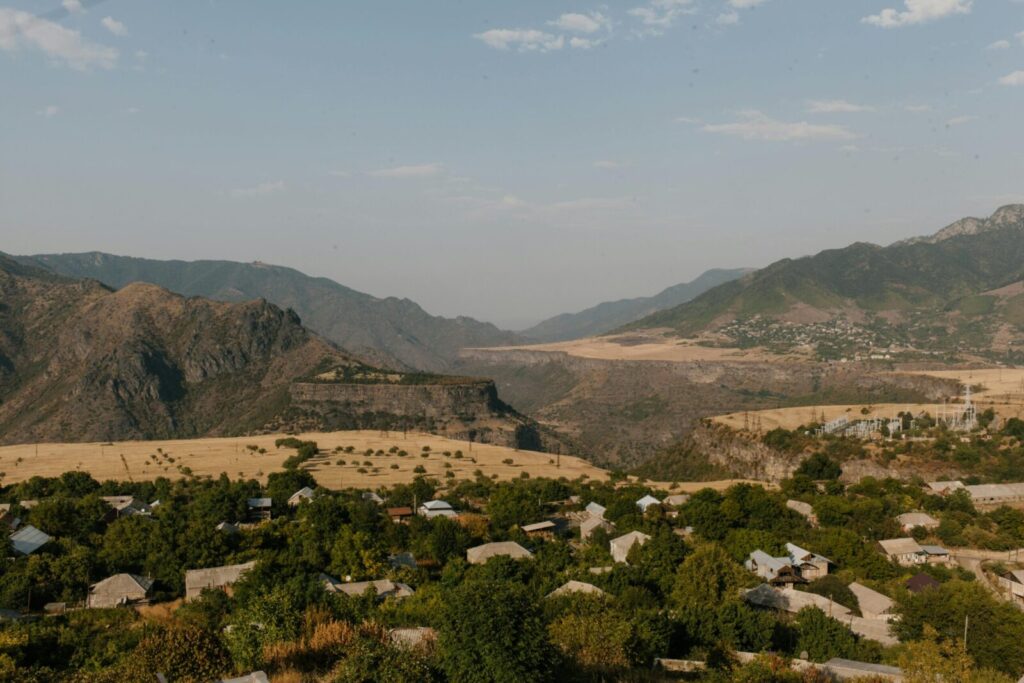 From above of residential buildings located among green trees surrounded by rocky mountains in village
